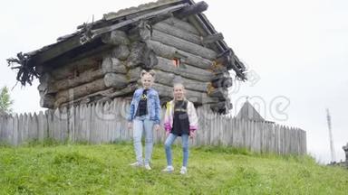 两个女孩少年站在绿色草坪上旋转童话屋。 少女在老巫婆的木屋上摆姿势